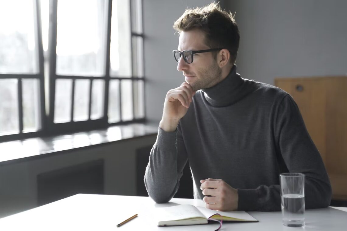man in an office wearing glasses looking away in thought