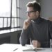 man in an office wearing glasses looking away in thought
